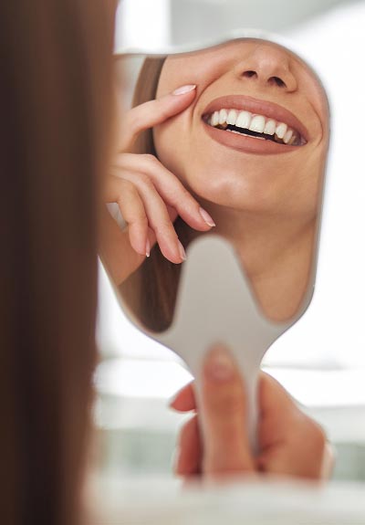 woman smiling in the mirror after getting services from Universal Dentistry in Cherry Hill, NJ